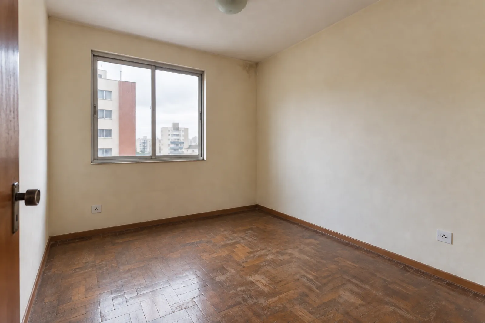 Quarto vazio antes da reforma, com piso antigo e manchas leves de umidade.
