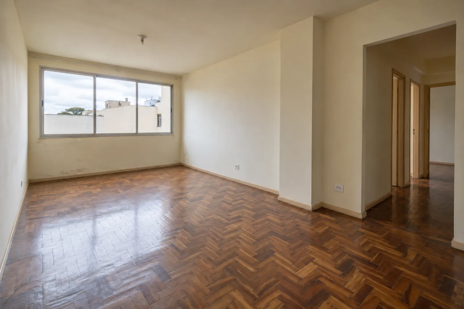 Sala vazia antes da reforma, com piso de taco gasto e pintura amarelada.